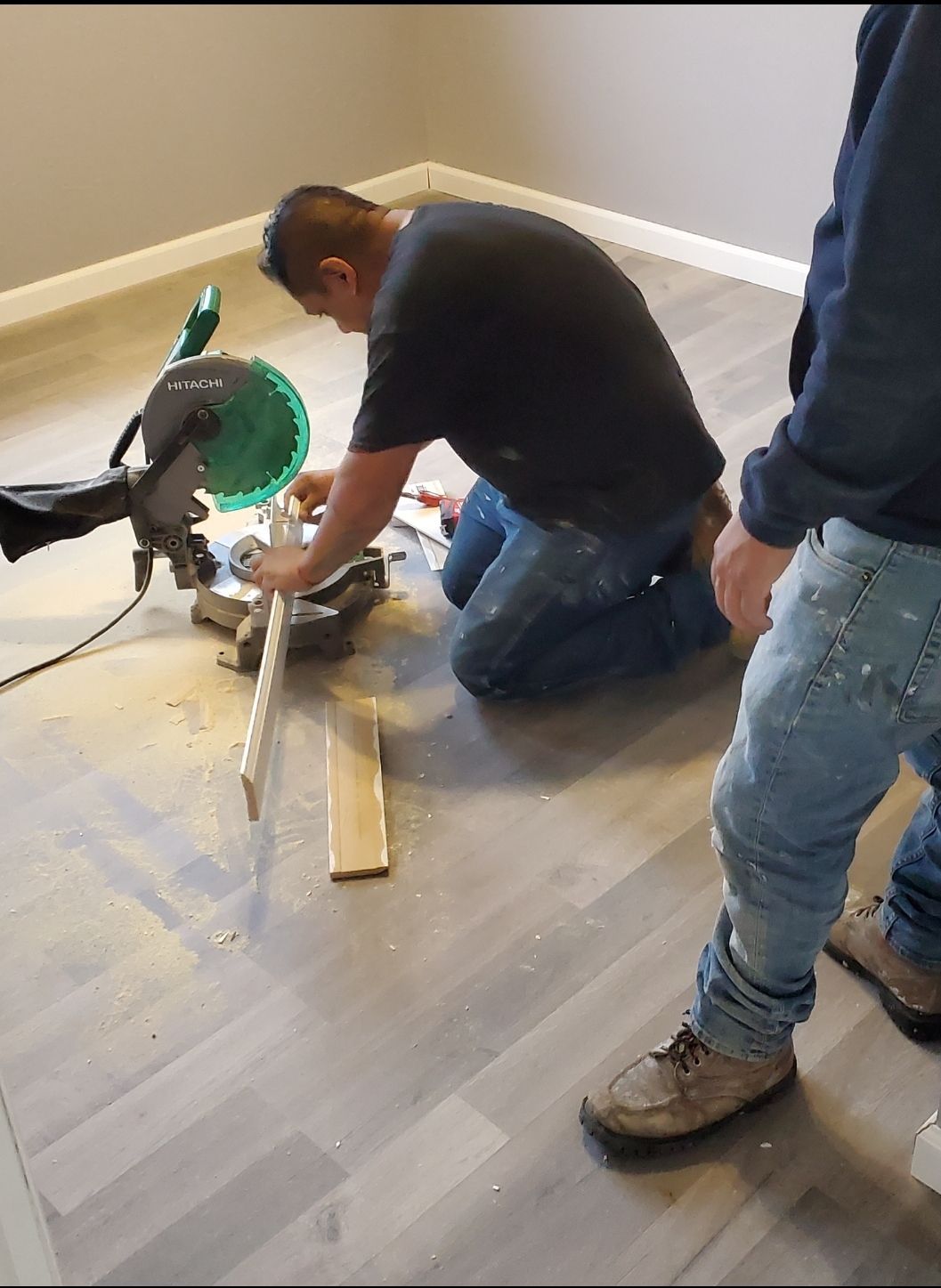A man is kneeling on the floor using a circular saw.