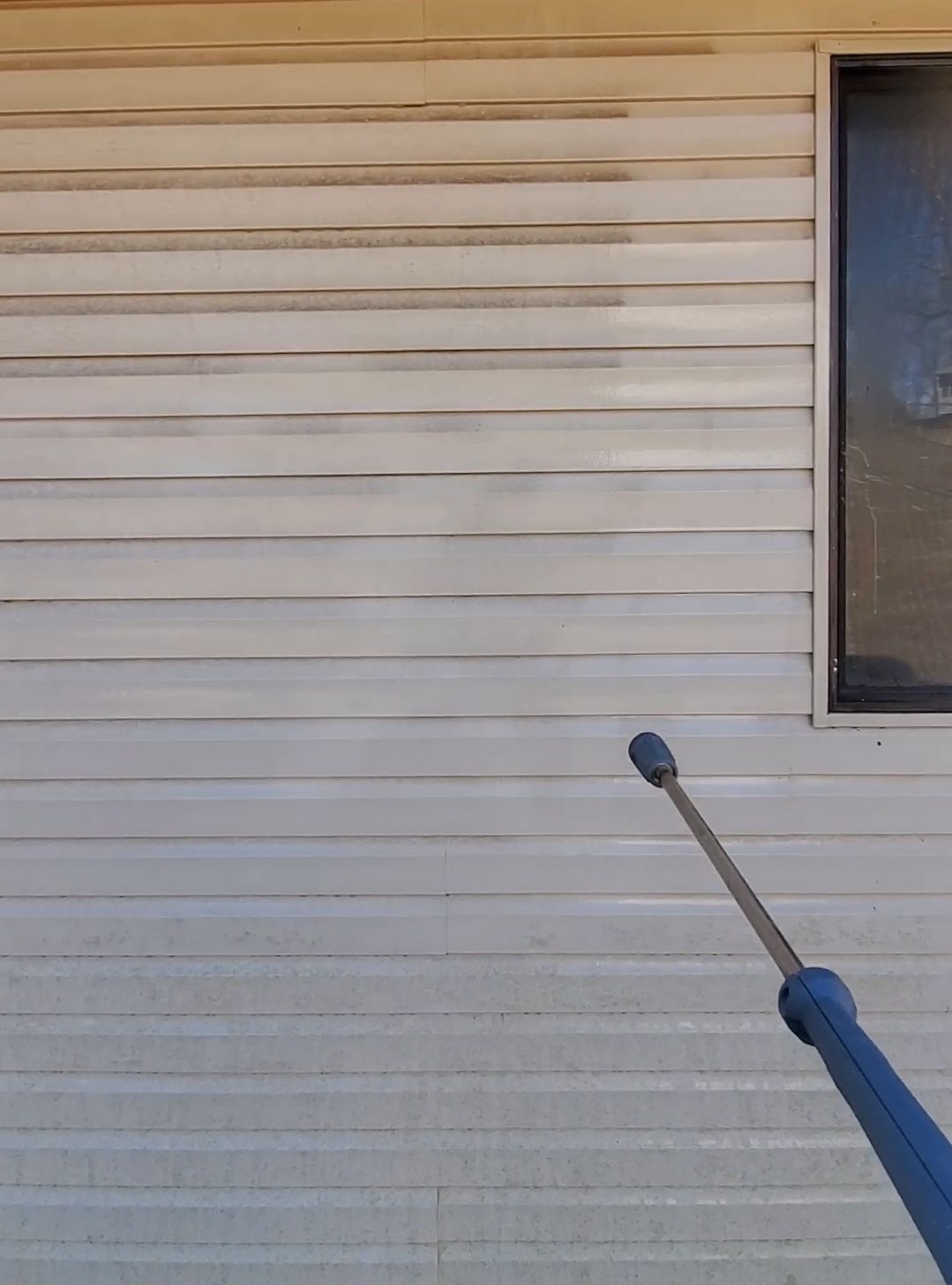 A person is cleaning the side of a house with a high pressure washer.