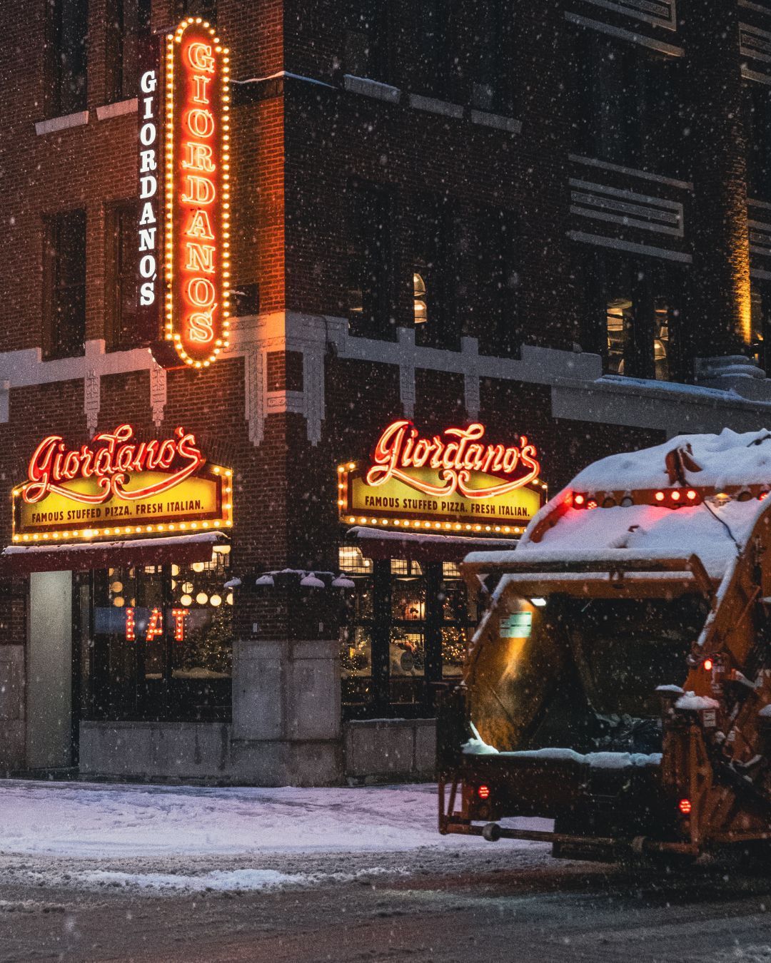 Giordano's restaurant in snowy weather, lit signs, brick building, snowplow in front.