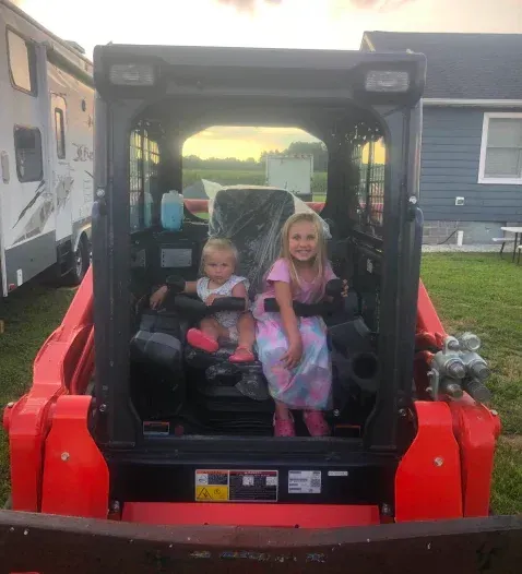 Two children are sitting in the back of a red bulldozer.