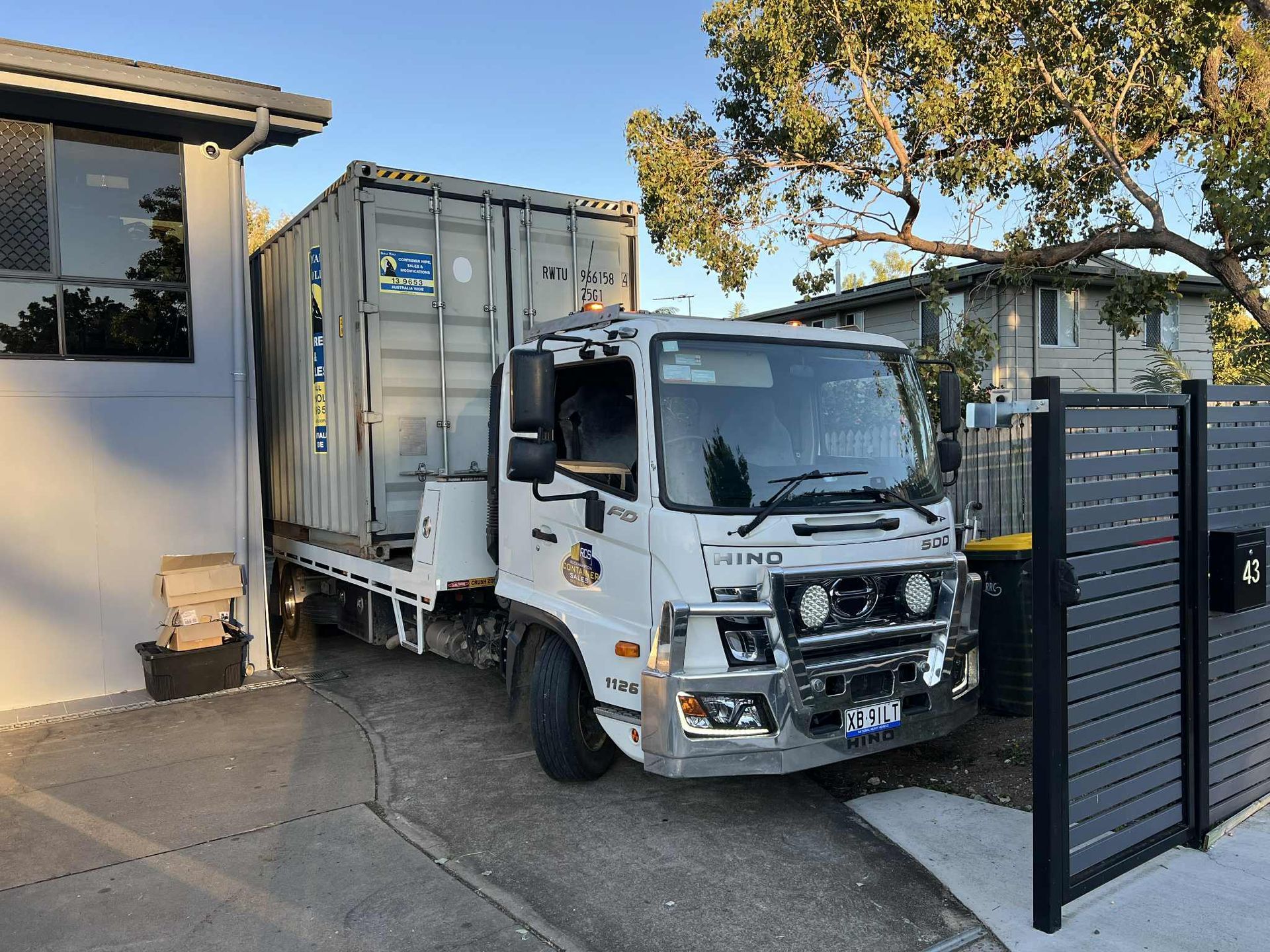 a Truck Carrying a Shipping Container Parked in a Residential Driveway — Rockhampton Container Sales in Kawana, QLD