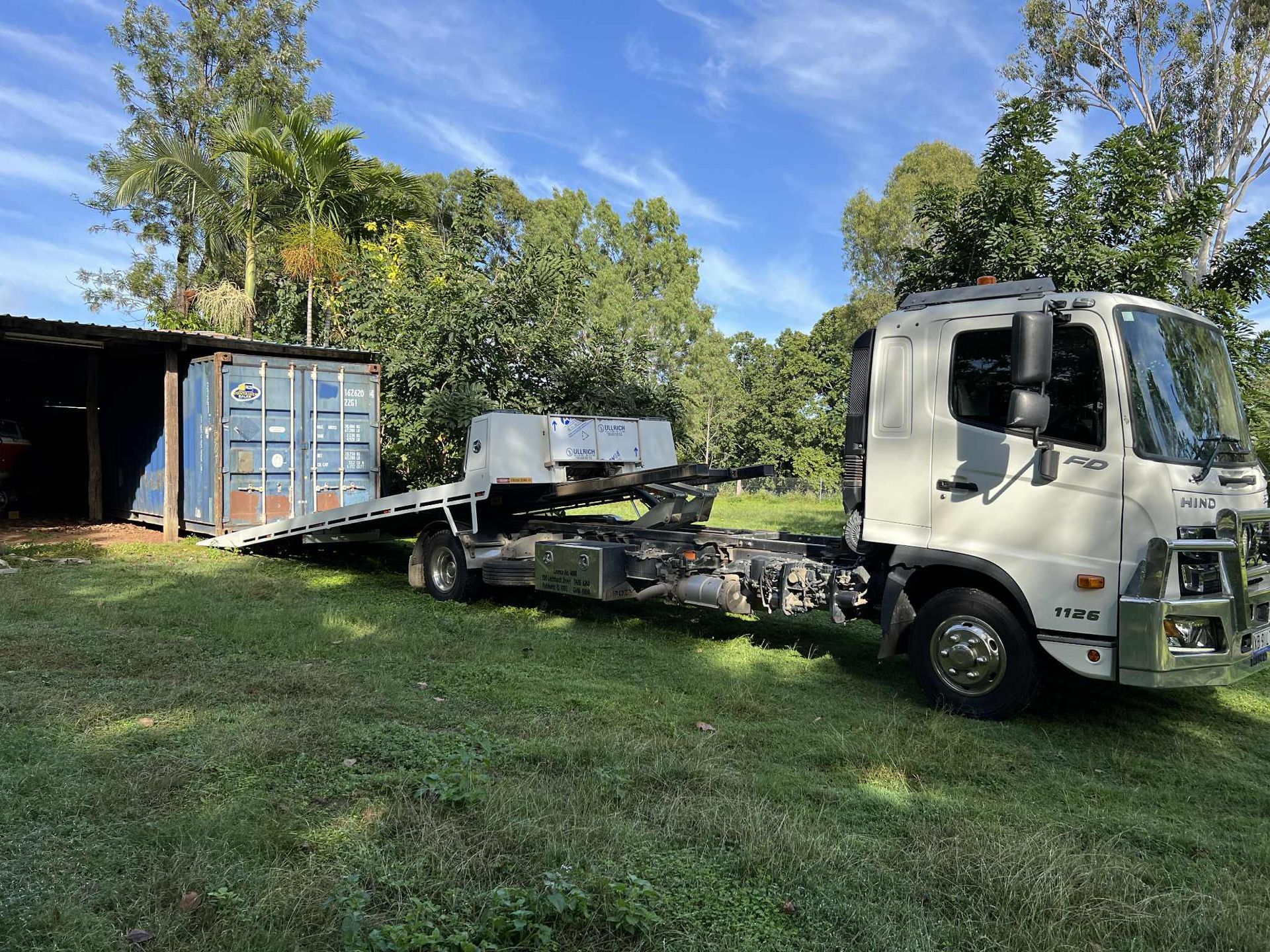 a White Truck With a Flatbed Trailer Next to a Blue Shipping Container  — Rockhampton Container Sales in Kawana, QLD
