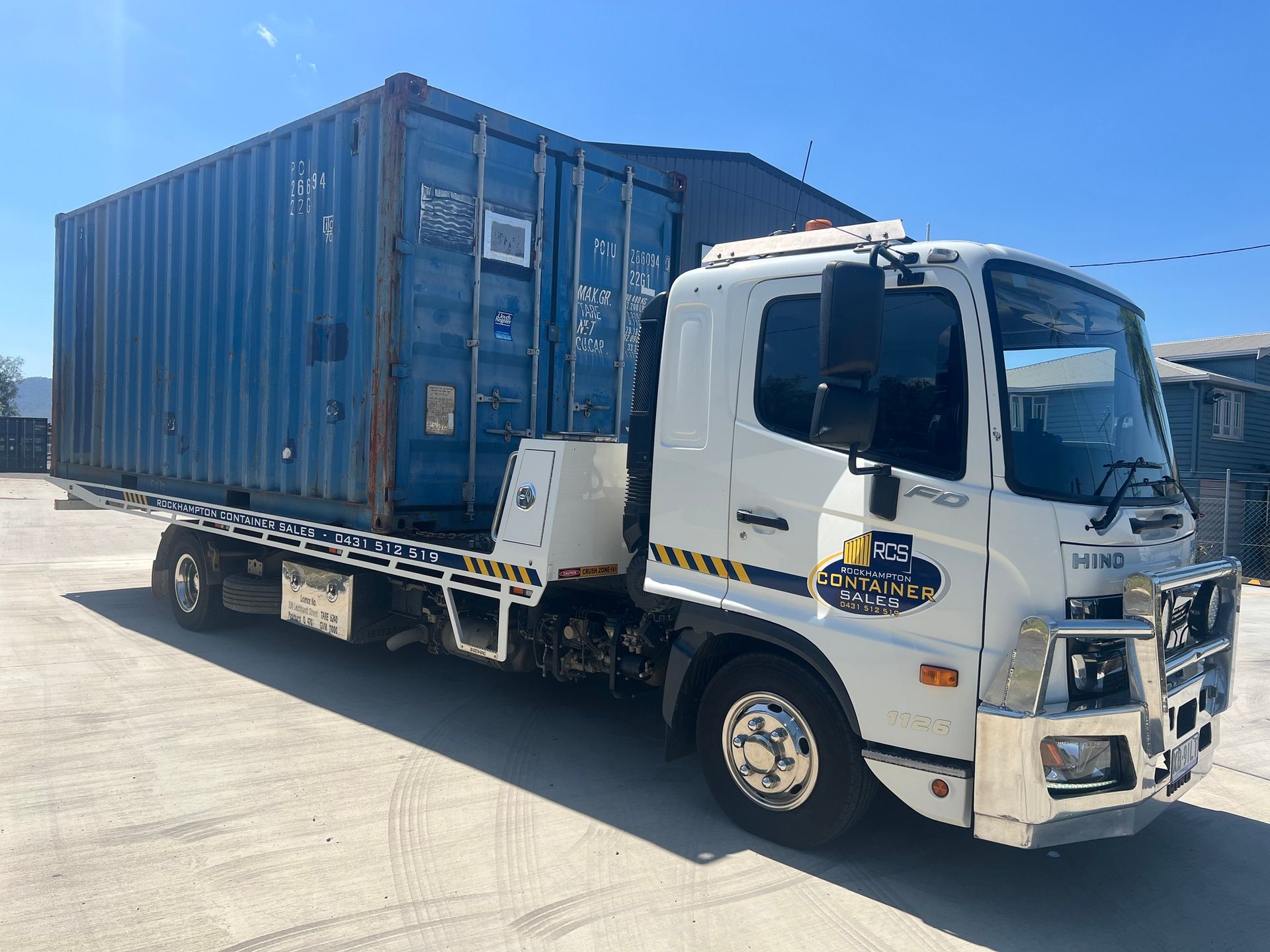 a Flatbed Truck Carrying a Blue Shipping Container on a Paved Surface  — Rockhampton Container Sales in Kawana, QLD