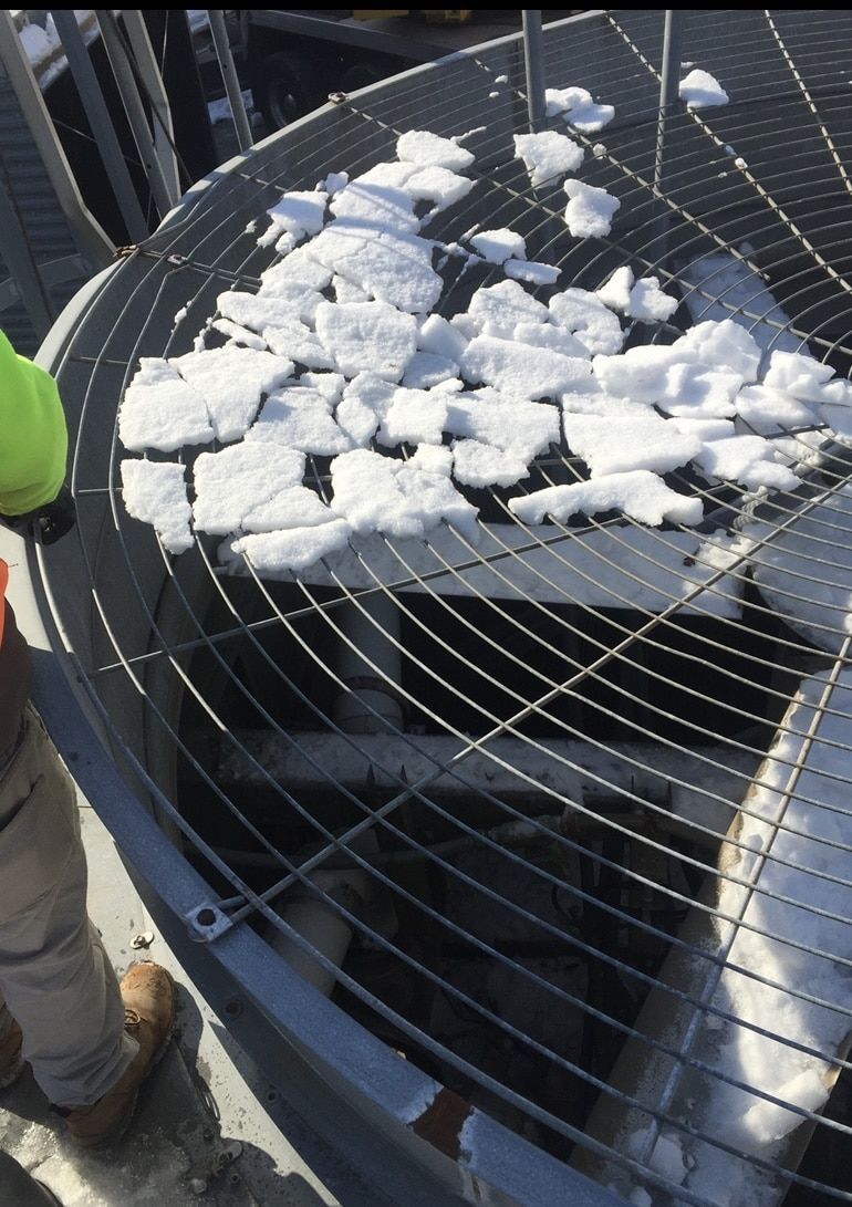 A person is standing next to an air conditioner with snow on it.