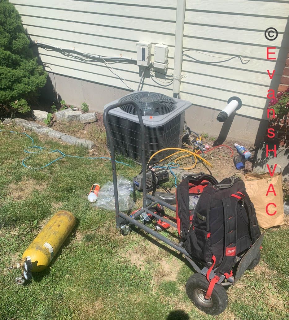 An air conditioner is sitting on a cart in the grass next to a house.