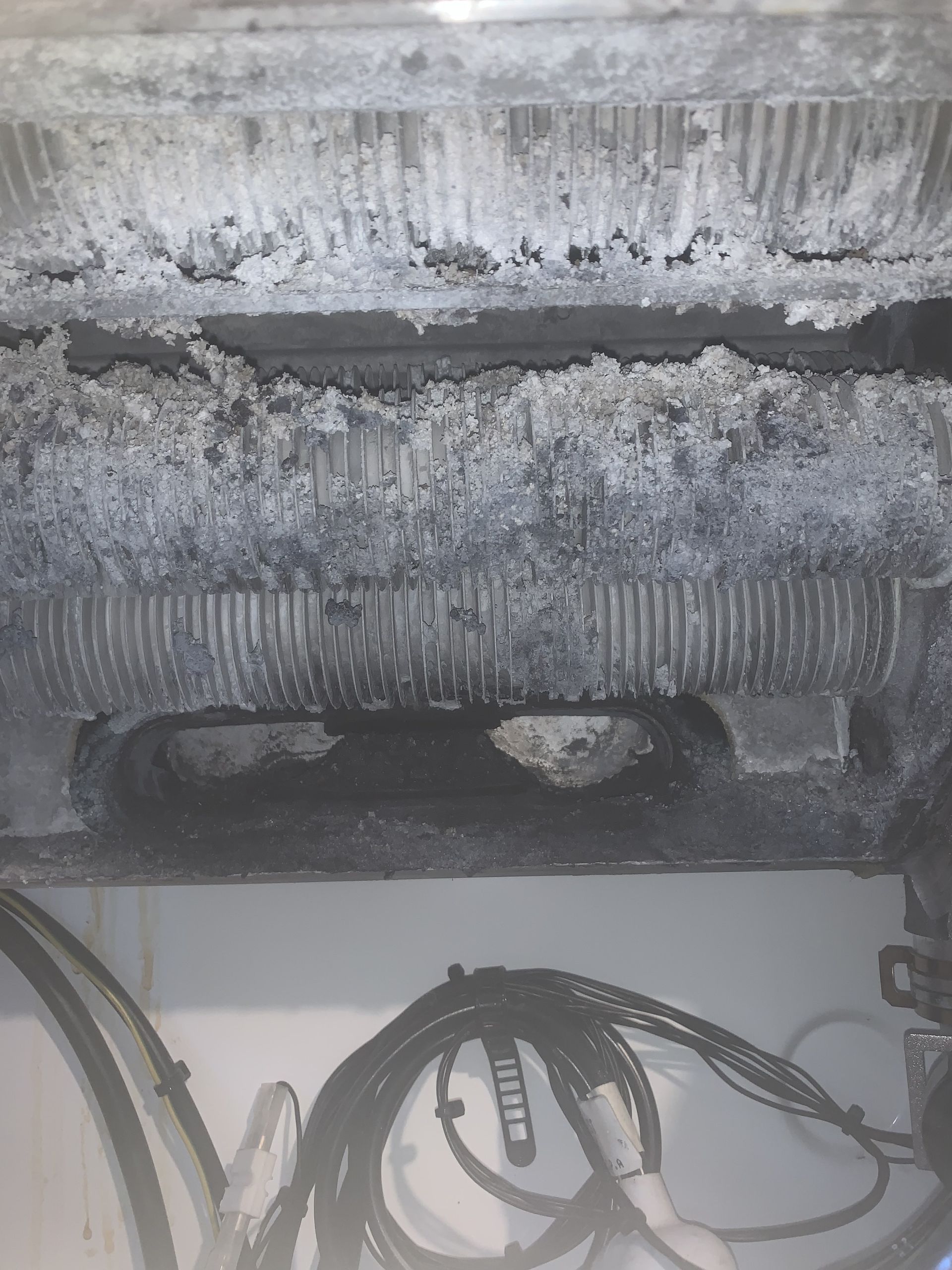 A black and white photo of a dirty refrigerator with a lot of wires coming out of it.