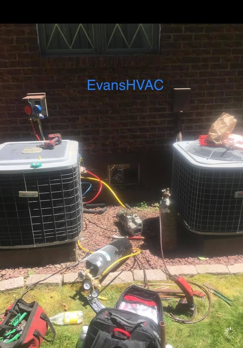 Two air conditioners are being repaired outside of a brick building.