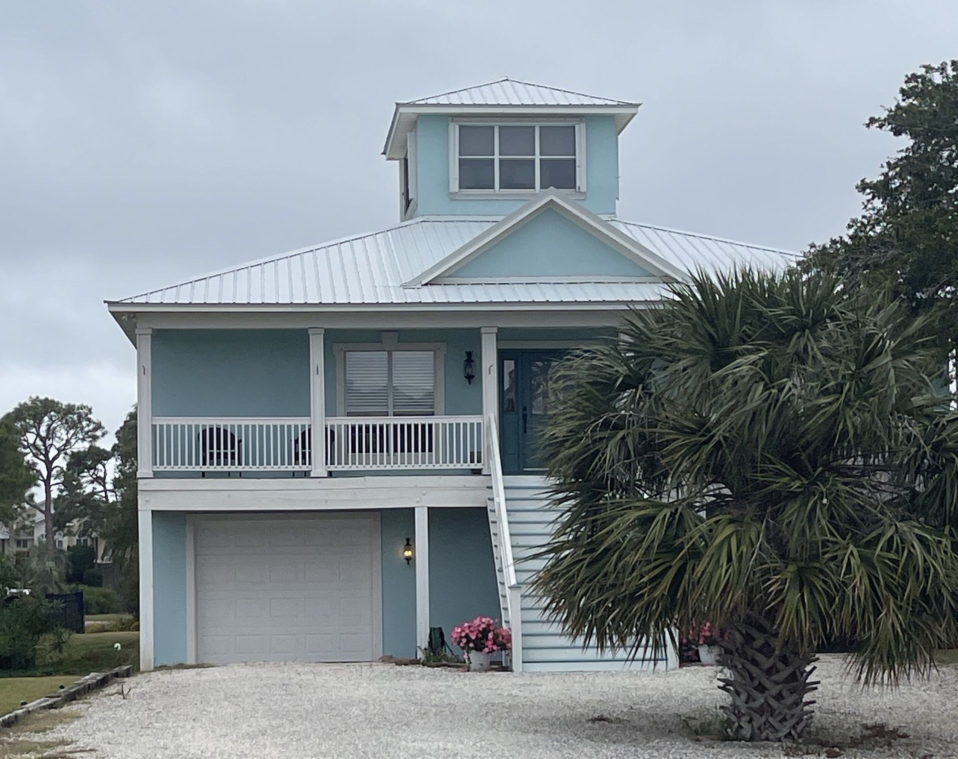 A blue house with a white garage door and a palm tree in front of it.