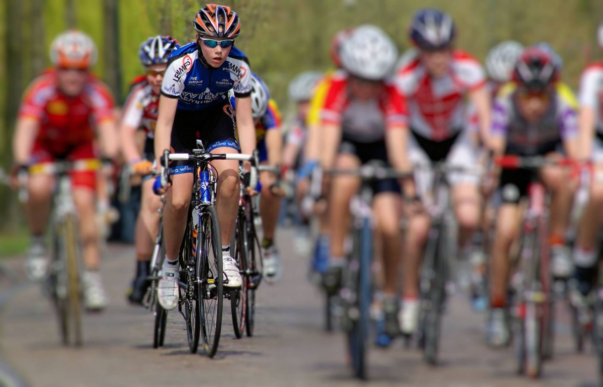Wielrenners racen op de weg; de renner in het blauwe shirt rijdt vooraan en is geconcentreerd.