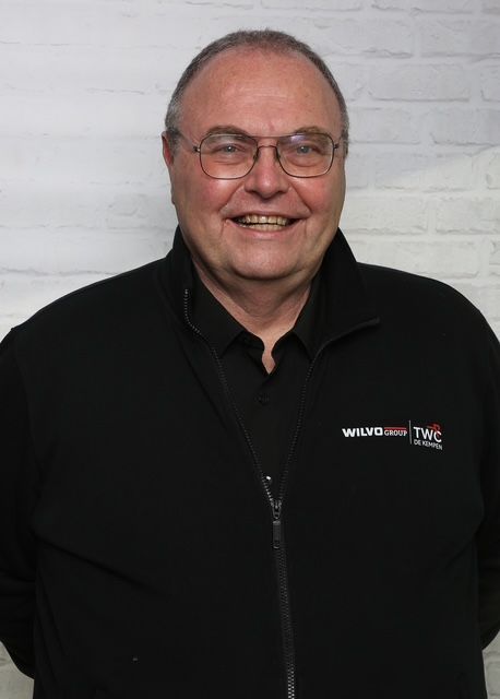 Vrouw met bruin haar lacht naar de camera, draagt ​​een lichtgekleurd shirt en staat voor een witte achtergrond.