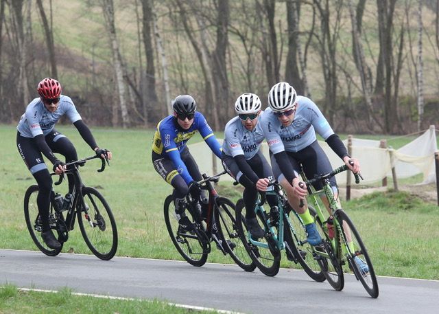 Wielrenners racen op de weg; de renner in het blauwe shirt rijdt vooraan en is geconcentreerd. 
