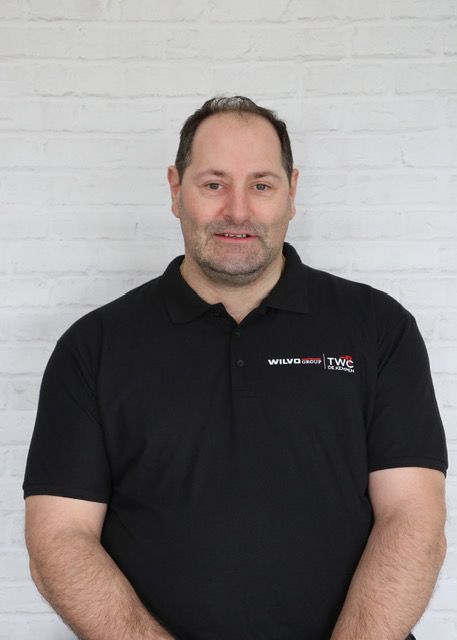 Vrouw met bruin haar lacht naar de camera, draagt ​​een lichtgekleurd shirt en staat voor een witte achtergrond.