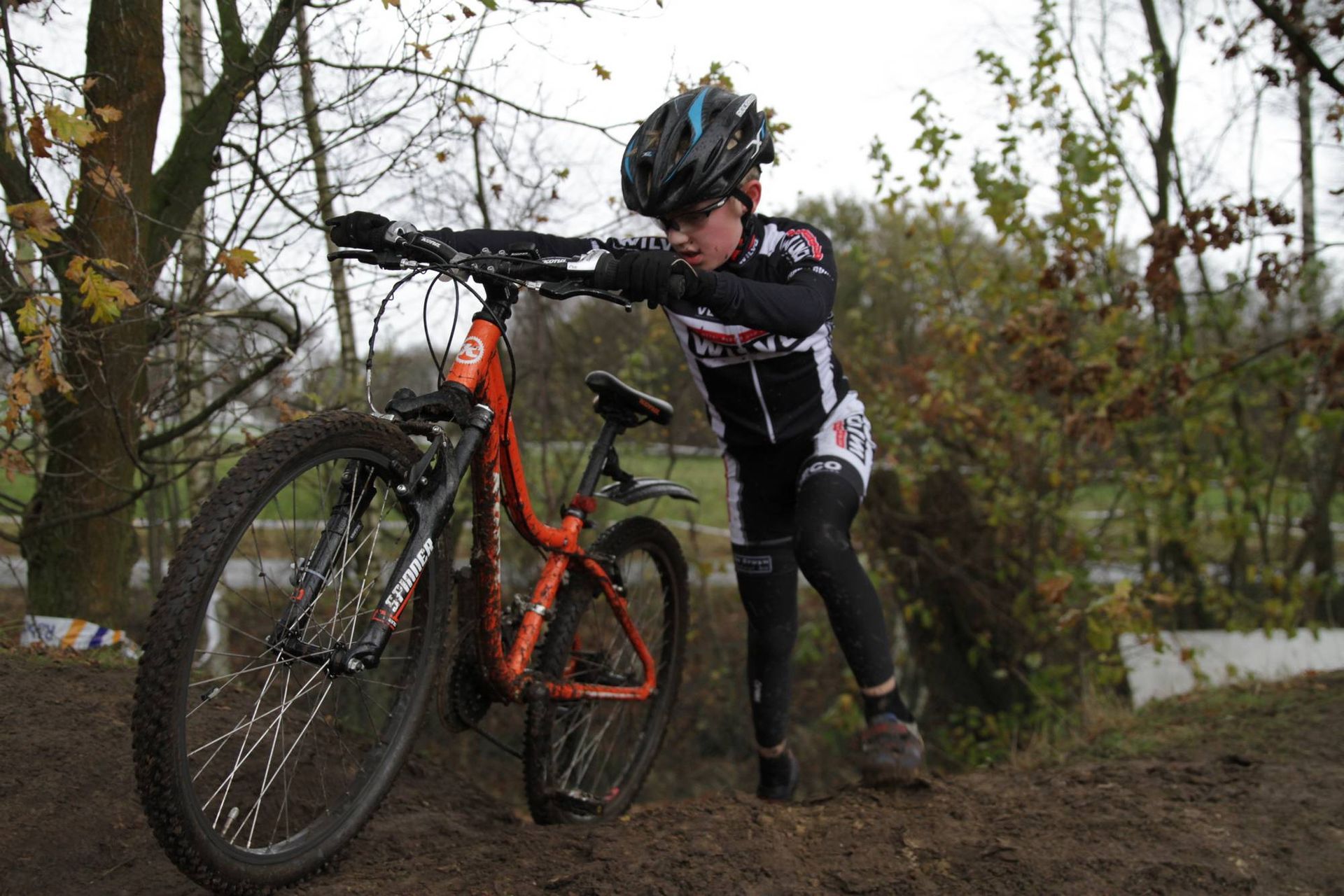 Een fietser in zwart-witte kleding worstelt om zijn oranje fiets door de modder te duwen.