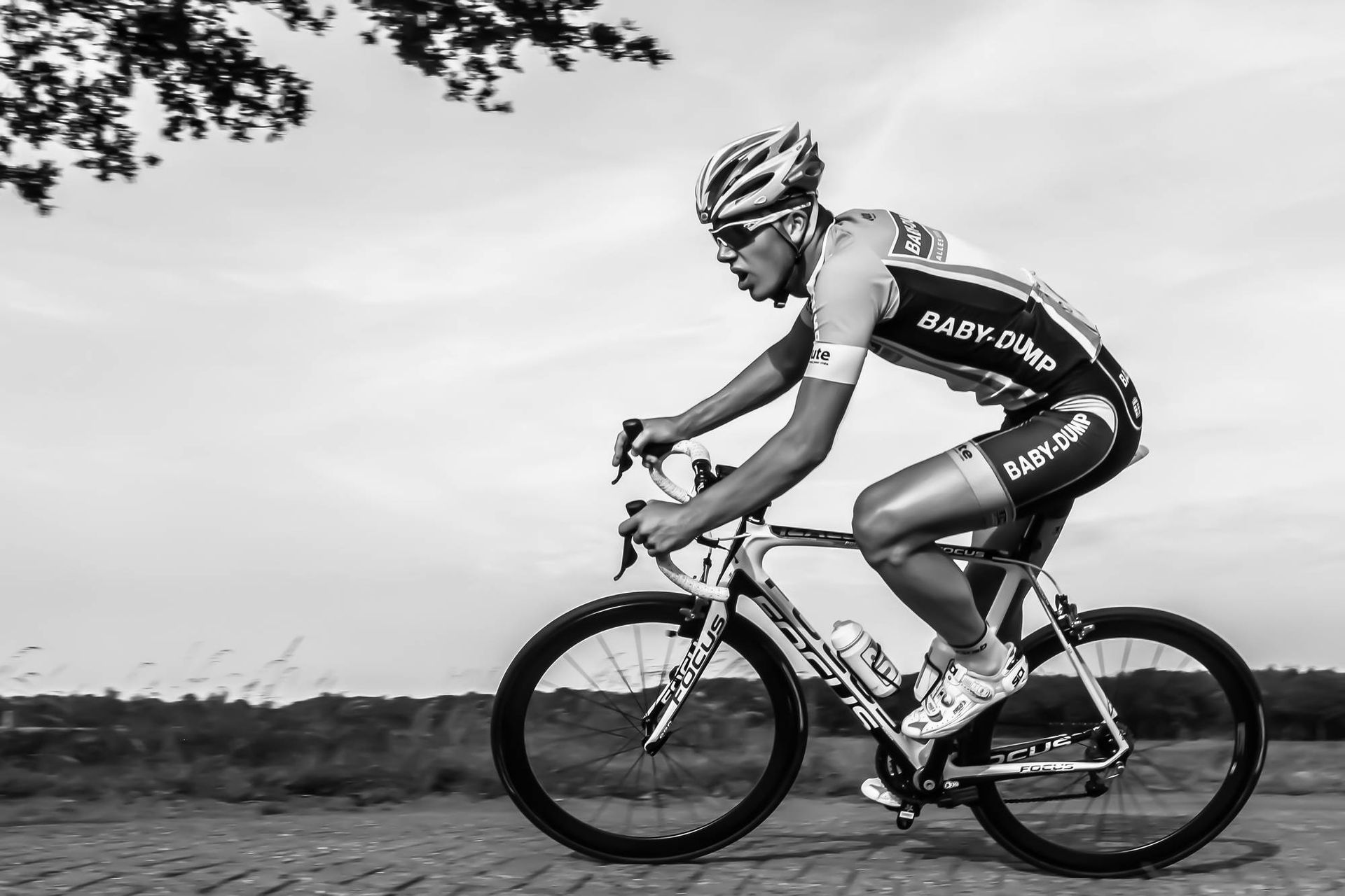 Een fietser in uniform rijdt op een racefiets over een geasfalteerde weg onder een bewolkte hemel.
