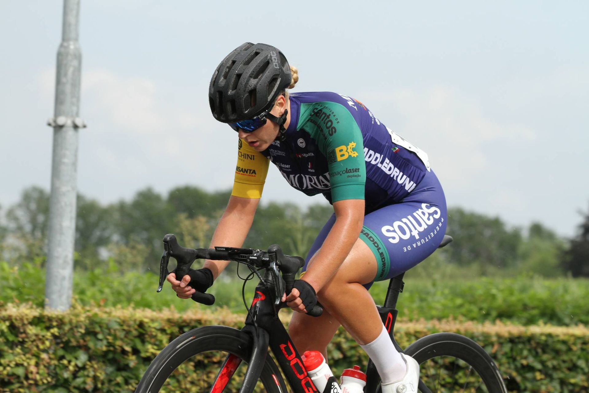 Fietser in blauwgroen uniform, rijdend op een fiets op een weg, voorovergebogen, met bomen op de achtergrond.