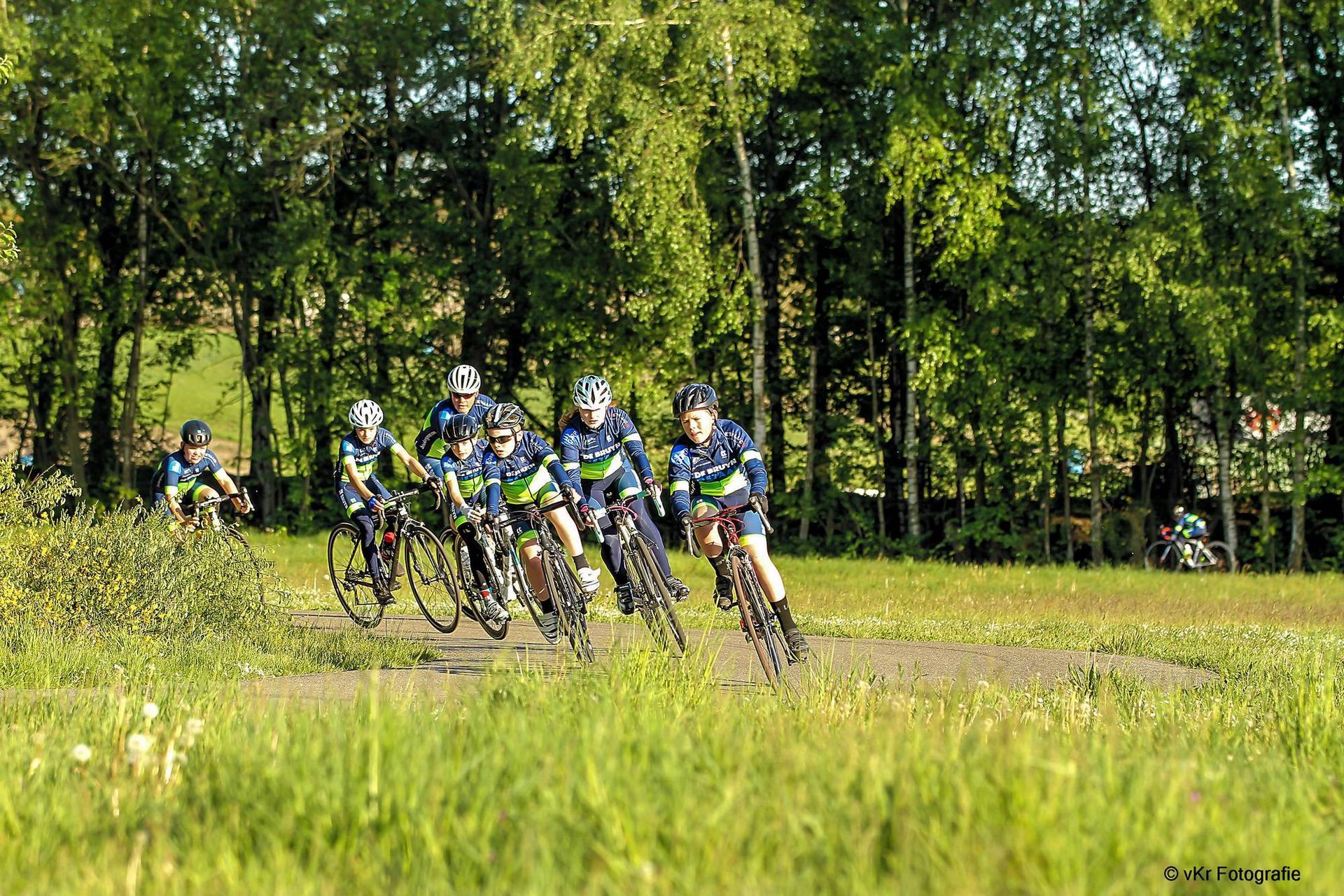 Wielrenners in bijpassende shirts op een onverhard pad in de buurt van bomen.