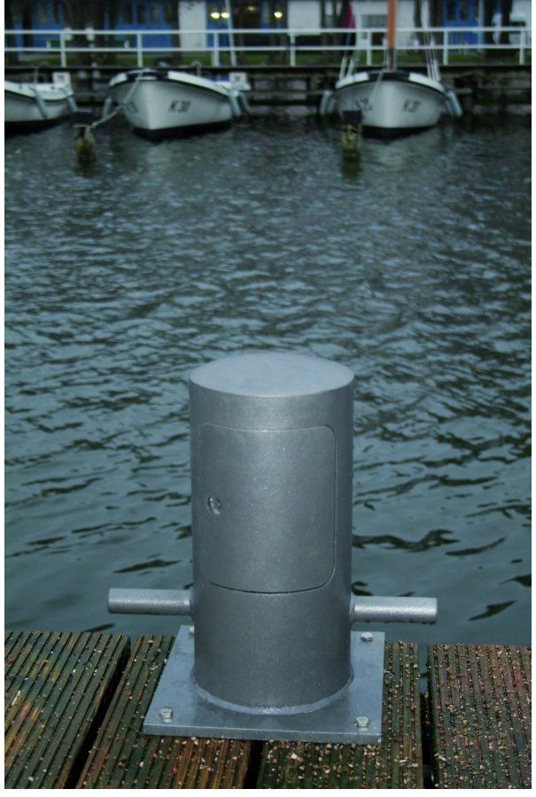 Mehrere Boote liegen in einem Hafen vor Anker, im Vordergrund ist ein grauer Mast zu sehen