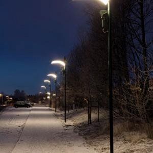 Eine Reihe von Straßenlaternen auf einem verschneiten Gehweg bei Nacht.