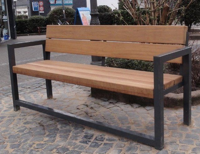 Eine Holzbank mit einem Metallrahmen steht auf einer Kopfsteinpflasterstraße