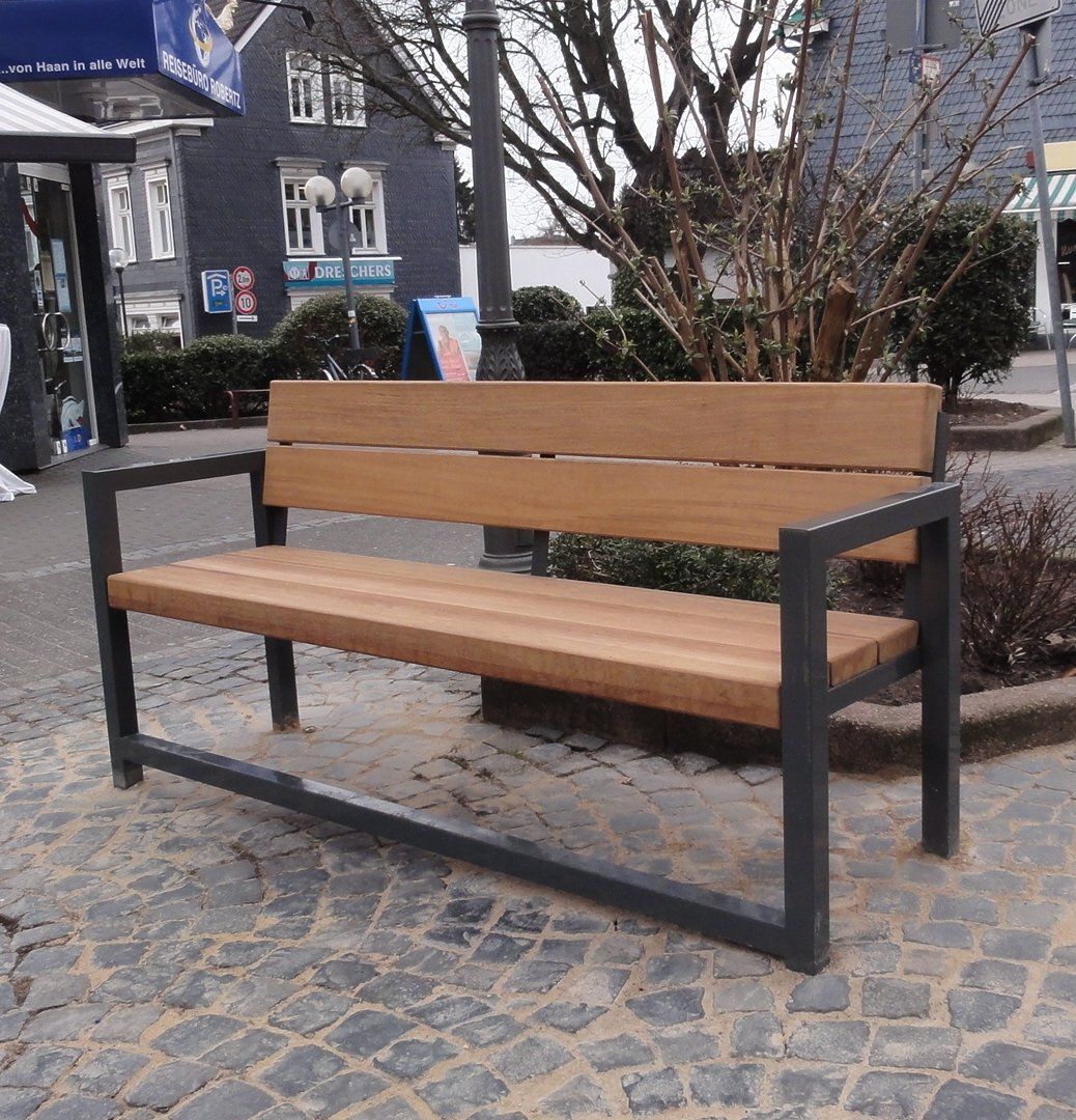Eine Holzbank mit einem Metallrahmen steht auf einer Kopfsteinpflasterstraße