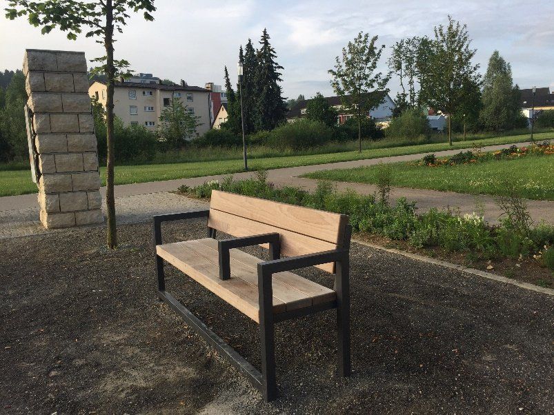 Eine Holzbank in einem Park mit einer gemauerten Säule im Hintergrund