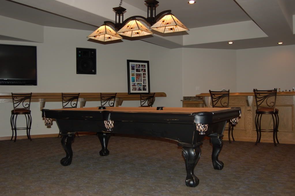 Pool table in a room with a bar and chairs; cream-colored walls and carpet.