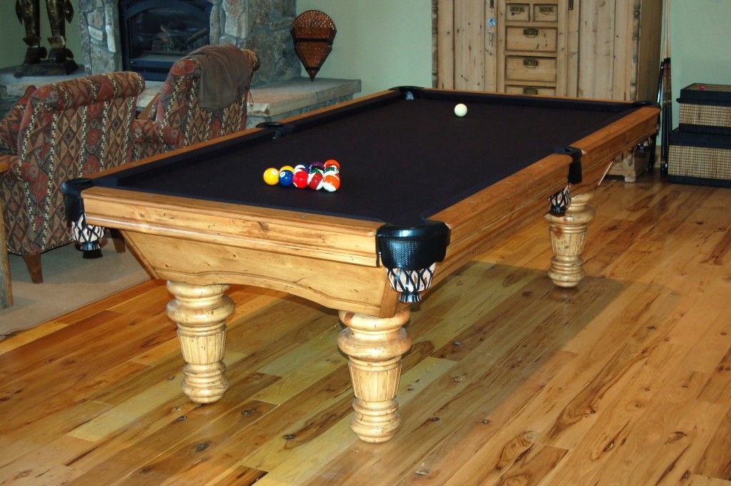 Pool table in a wood-floored room, balls racked and one in play.