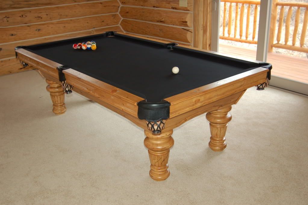 Pool table with black felt and wooden frame, balls arranged, in a room with wood paneling.