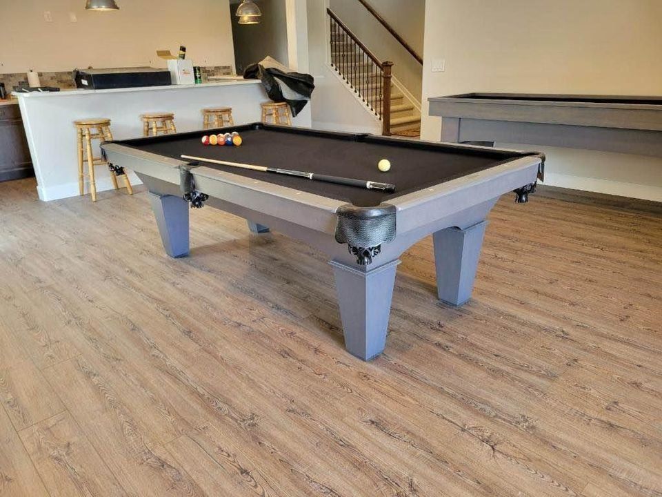 Pool table in a home basement, with balls and a cue stick on it.