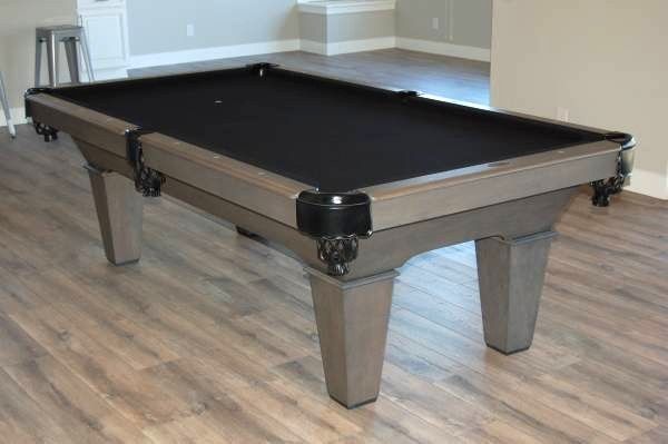Gray pool table with black felt on wood floor.