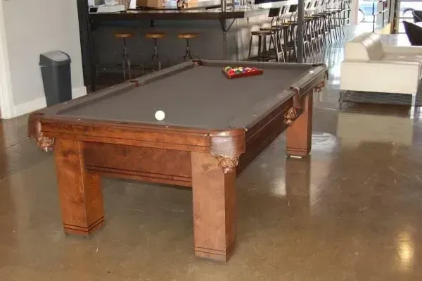 Pool table with balls on a brown wooden table in a room with a bar in the background.