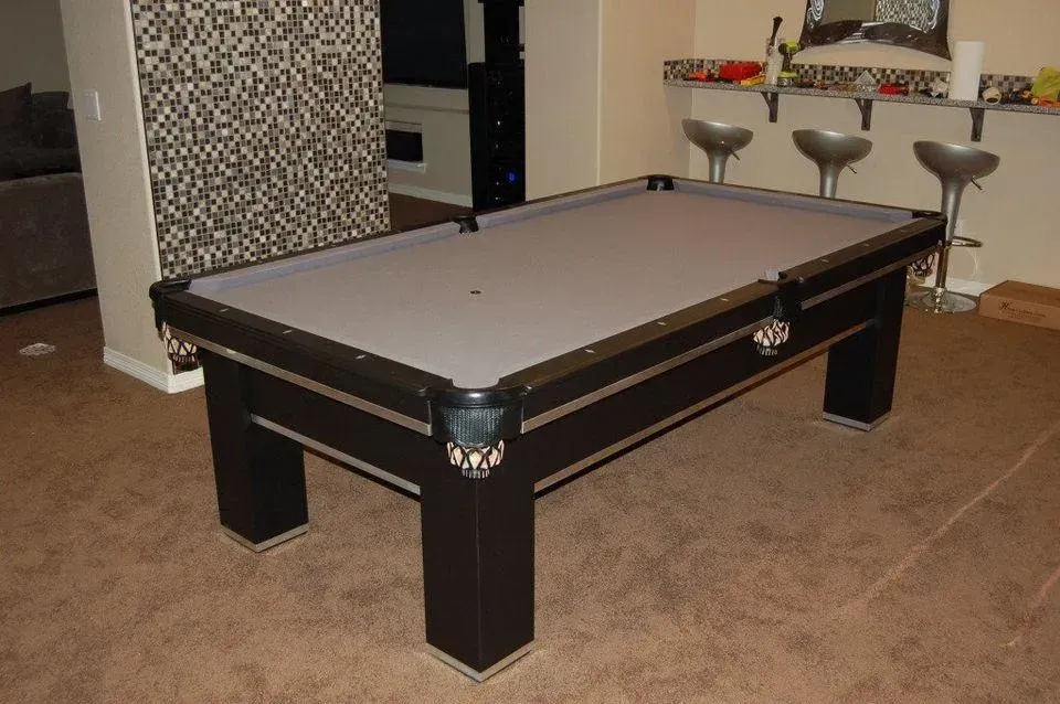 A black pool table with gray felt in a room with a bar and stools.