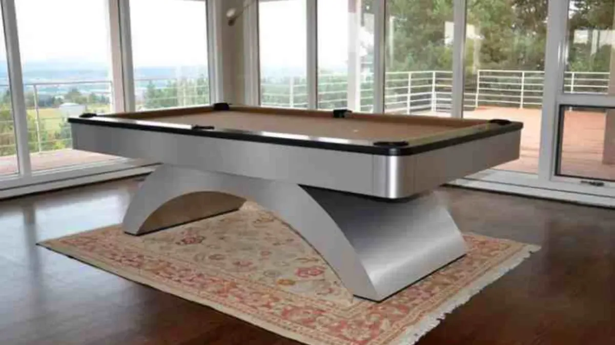 Modern silver pool table on a patterned rug, set in a room with large windows overlooking a scenic landscape.