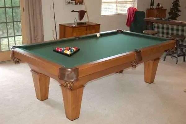 Pool table with a green felt surface and wooden frame, balls racked in a triangle.