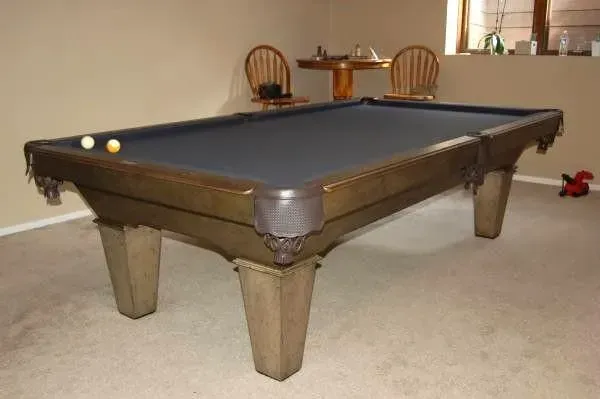 Pool table in a room with two balls on the felt. Two chairs and a small table are in the background.