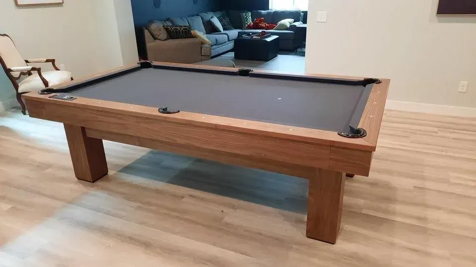 Wooden pool table with gray felt in a room with light wood floors.