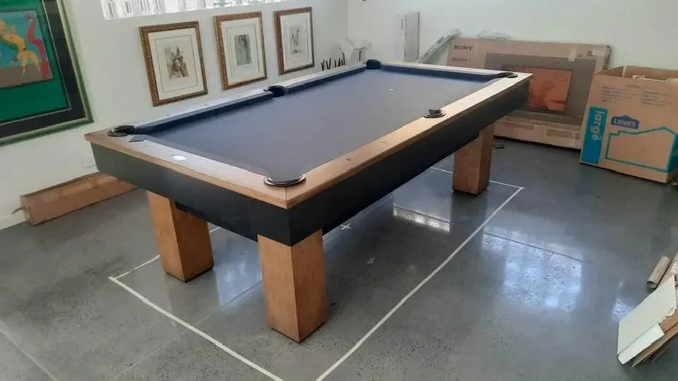 Pool table with a blue felt top, set in a room with paintings and moving boxes.