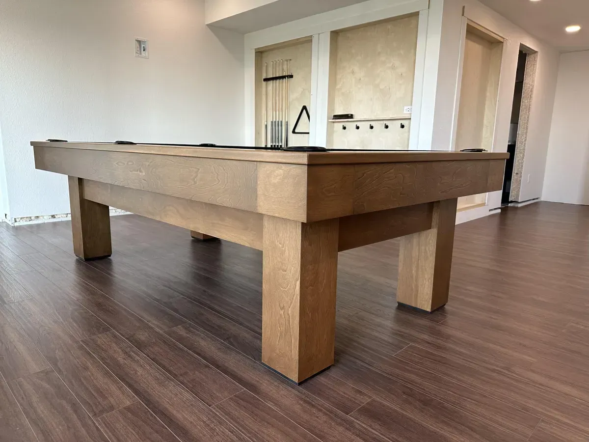 Wooden pool table with dark felt top in a room with hardwood floors.