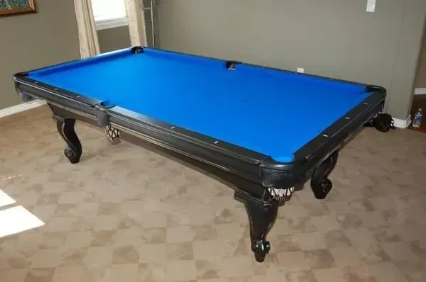 Black pool table with blue felt, ornate legs, in a room with tan carpet and gray walls.