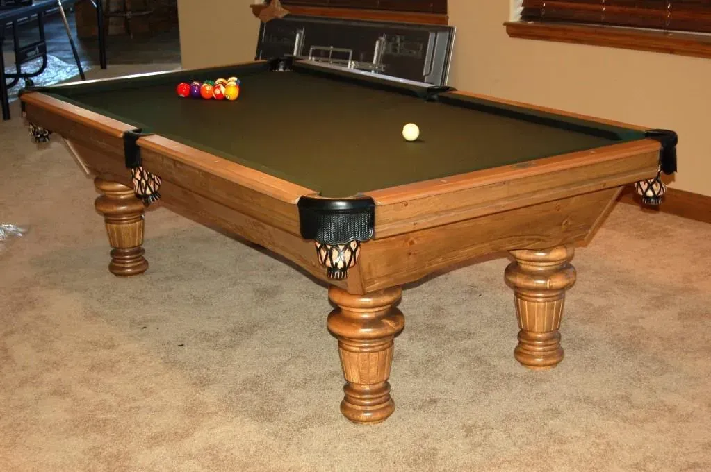 Pool table with balls on green felt in a room with hardwood trim and carpet.