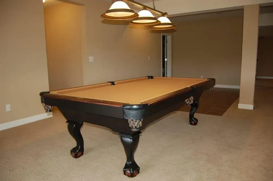 Pool table in a beige-walled room with a pendant light fixture overhead, resting on carpeted flooring.