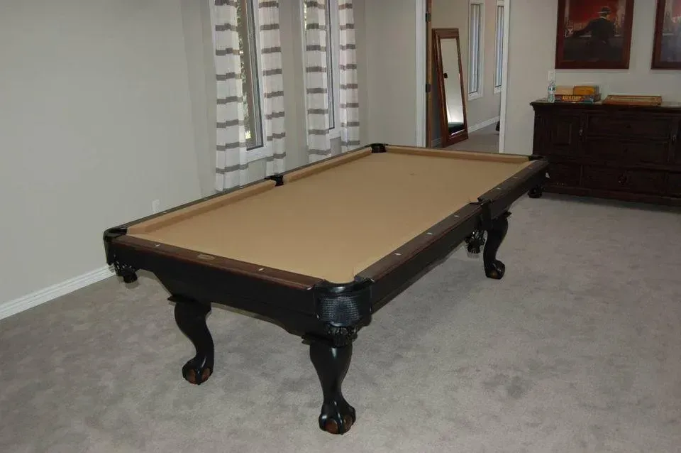 Pool table in a room with a tan felt surface, black wood frame, and claw feet.