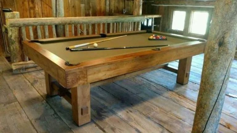 Wooden pool table in rustic room with cues and balls.