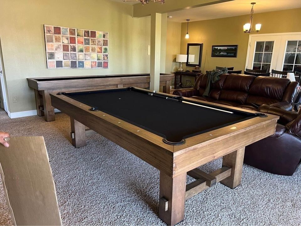 A wood pool table with a black felt surface sits in a room with a ping-pong table and a leather couch.