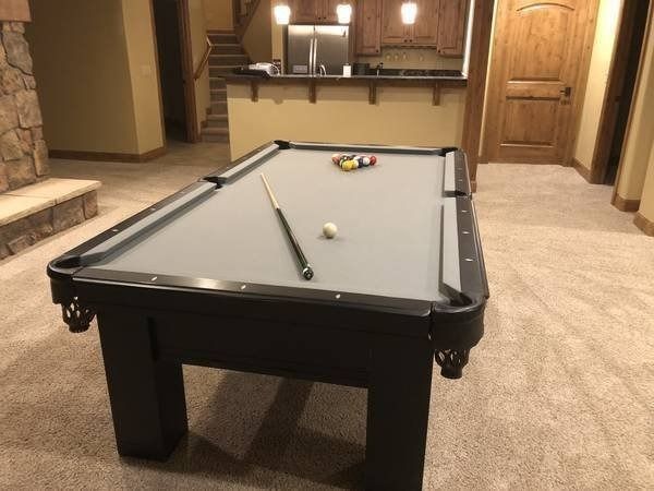 Pool table in a game room with balls, a cue, and a bar area.