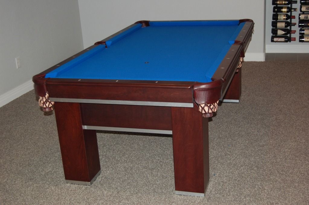 A wooden pool table with blue felt sits on a carpeted floor.