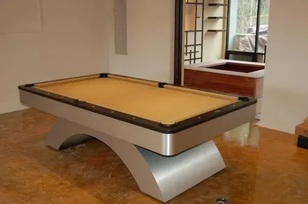 A modern silver and black pool table with a tan felt surface in a room with a concrete floor.