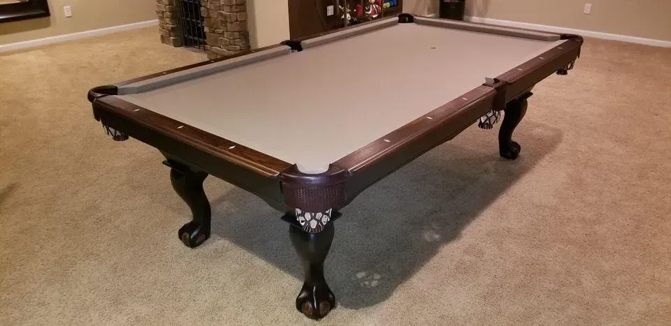 A pool table with a tan felt top and dark wood frame, resting on a carpeted floor.