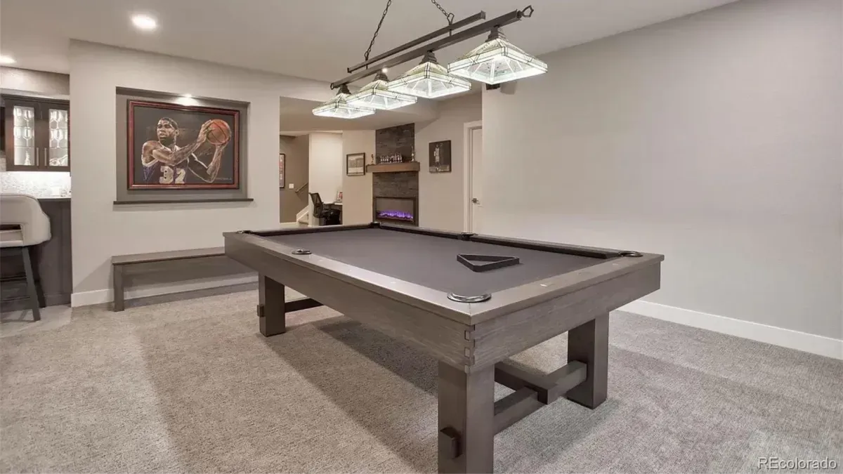 Pool table in a game room with gray walls, carpet, and a light fixture.