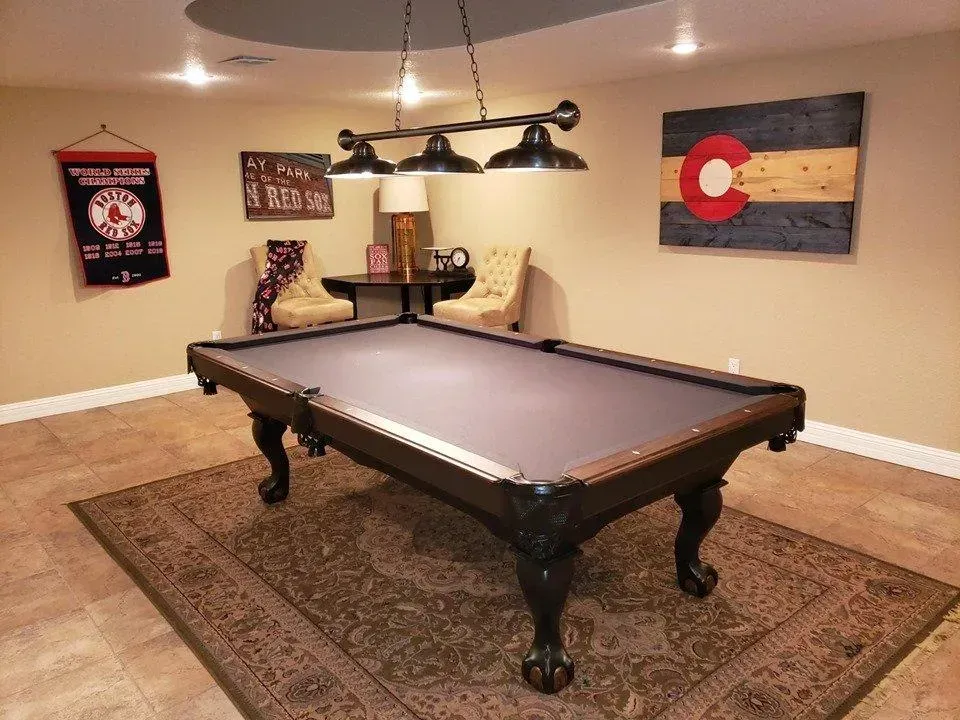 Pool table in a game room with decorative lights, rug, and Colorado flag art.